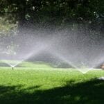 A couple of water sprinklers spraying on some grass.