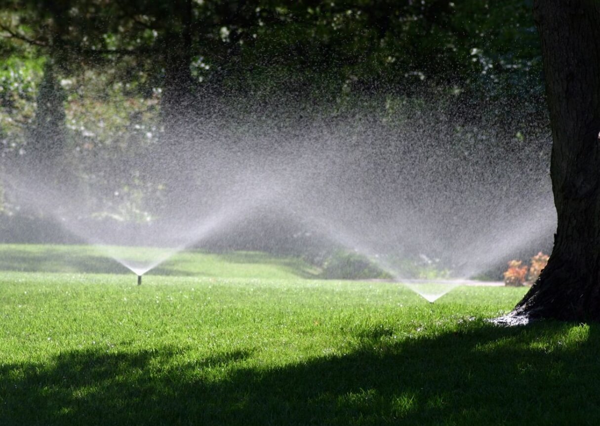 A couple of water sprinklers spraying on some grass.
