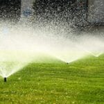 A lawn with sprinklers spraying water on it.